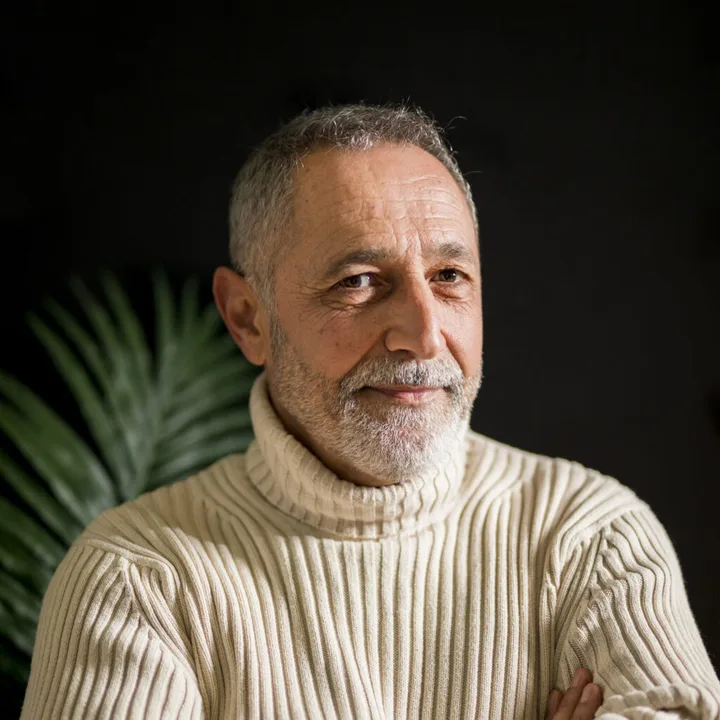 A man with gray hair in a cream turtleneck sweater